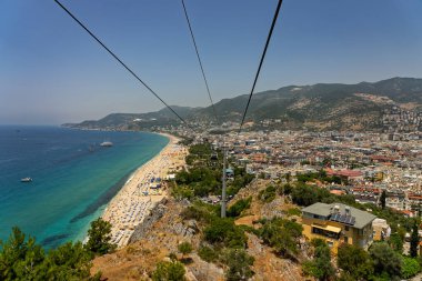 Alanya şehrinin insansız hava aracı görüntüsü, Türkiye. Sahil şeridi, Akdeniz, liman, tepenin üzerindeki tarihi şato ve açık bir yaz gününde arka planda dağların olduğu geniş kentsel alan. Alanya, Türkiye.