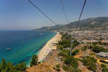 Alanya şehrinin insansız hava aracı görüntüsü, Türkiye. Sahil şeridi, Akdeniz, liman, tepenin üzerindeki tarihi şato ve açık bir yaz gününde arka planda dağların olduğu geniş kentsel alan. Alanya, Türkiye.