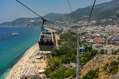 Alanya şehrinin insansız hava aracı görüntüsü, Türkiye. Sahil şeridi, Akdeniz, liman, tepenin üzerindeki tarihi şato ve açık bir yaz gününde arka planda dağların olduğu geniş kentsel alan. Alanya, Türkiye.