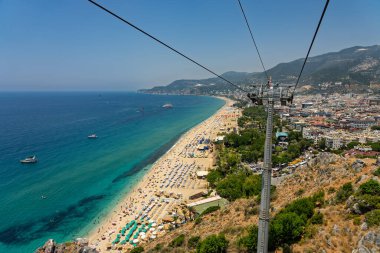 Alanya şehrinin insansız hava aracı görüntüsü, Türkiye. Sahil şeridi, Akdeniz, liman, tepenin üzerindeki tarihi şato ve açık bir yaz gününde arka planda dağların olduğu geniş kentsel alan. Alanya, Türkiye.