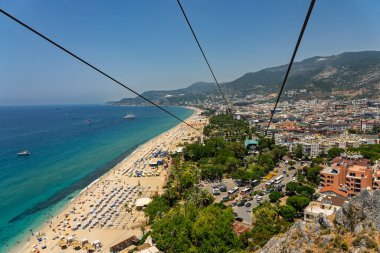 Alanya şehrinin insansız hava aracı görüntüsü, Türkiye. Sahil şeridi, Akdeniz, liman, tepenin üzerindeki tarihi şato ve açık bir yaz gününde arka planda dağların olduğu geniş kentsel alan. Alanya, Türkiye.