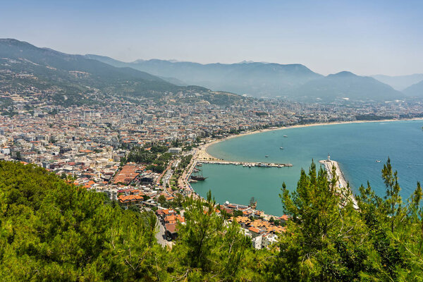 Drone view of Alanya city, Turkey. Coastline, Mediterranean Sea, harbor, historic castle on the hill, and sprawling urban area with mountains in the background on a clear summer day. Alanya, Turkey.