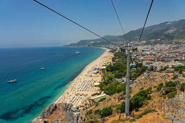 Alanya şehrinin insansız hava aracı görüntüsü, Türkiye. Sahil şeridi, Akdeniz, liman, tepenin üzerindeki tarihi şato ve açık bir yaz gününde arka planda dağların olduğu geniş kentsel alan. Alanya, Türkiye.