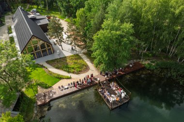 Göl kenarındaki düğün töreninin havadan görünüşü, konuklar yemyeşil ormanlarla çevrili ahşap bir rıhtımda ve terasta toplandılar..