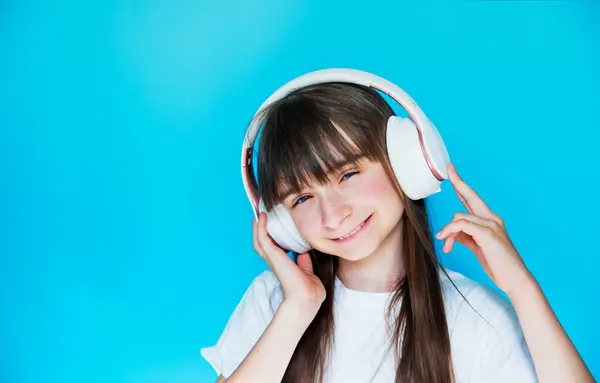 Sevimli genç kız kablosuz kulaklıkla müzik dinliyor ve dans ediyor. Mavi arka planda küçük bir DJ. Müziğe dalmak. Hobi olarak. Cep telefonuyla iletişim.