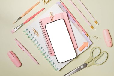 Yeşil arka planda cep telefonu ve pembe okul malzemeleri. Okula dönelim. Düz yerde, üst tarafta. Kompozisyonun ortasına uzayı kopyala.