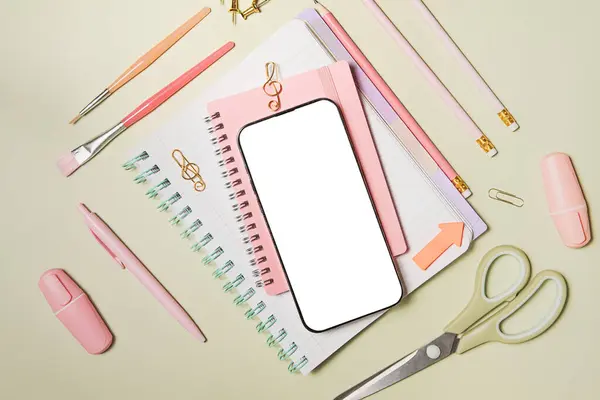 Yeşil arka planda cep telefonu ve pembe okul malzemeleri. Okula dönelim. Düz yerde, üst tarafta. Kompozisyonun ortasına uzayı kopyala.