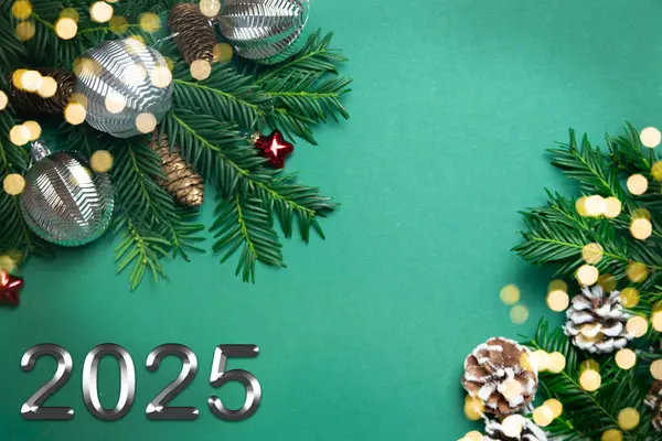 Noel ve 2025 yılbaşı konsepti. Canlı köknar dallarından, çam kozalaklarından ve yeşil arka planda gümüş Noel toplarından yapılan dekorasyonun en üst görüntüsü. Boşluğu kopyala.