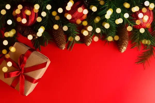 Noel ve Yeni Yıl konsepti. Köknar dalları, çam kozalakları, hediye kutusu ve kırmızı arka planda kırmızı Noel topları. Uzayı kopyala Şenlik arka planı. Tebrik kartı.