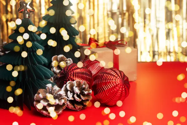Kağıt Noel ağaçlarından, kozalaklardan ve altın ve kırmızı arka planda kırmızı toplardan yapılmış şenlik süslemeleri. Mutlu yıllar 2025 tebrik kartı..