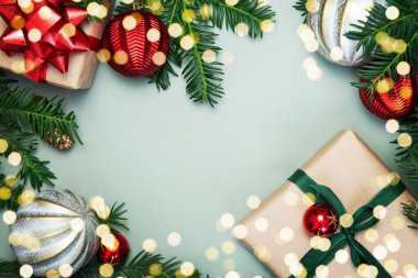 Köknar dalları, çam kozalakları, kırmızı ve gümüş toplar için şenlikli çerçeve dekorasyonu yeşil arka planda yeşil ve kırmızı kurdeleli kraft kağıdına doldurulmuş hediye kutuları. Noel ve Yeni Yıl. Boşluğu kopyala.