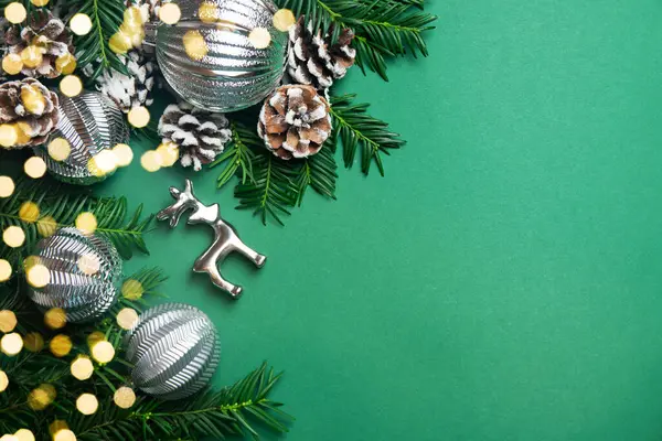 Köknar dallarının, kozalakların, gümüş geyiklerin ve yeşil arka plandaki Noel toplarının en üst görünümü. Boşluğu kopyala.