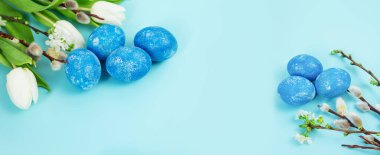Paskalya bayramı arkaplanı, taze beyaz laleler, boyanmış yumurtalar, çiçek açan dallar ve mavi arka planda söğüt ağacı. Boşluğu kopyala.