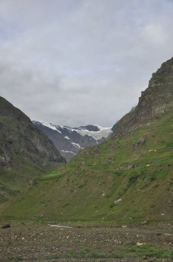 Lahaul ve Spiti, Himachal Pradesh, Hindistan 'da bulutlu havada, ağaçsız yeşil dağlar arasındaki buzullu dağ manzarası. 