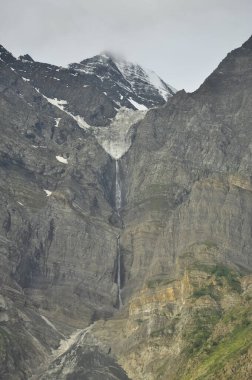 Bulutlu bir havada, kayalık dağın tepesinden düşen karların ve suyun güzel manzarası.