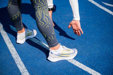 Bir bayan sporcunun mavi bir pistte koşmaya hazırlanırken yakın plan çekimi.