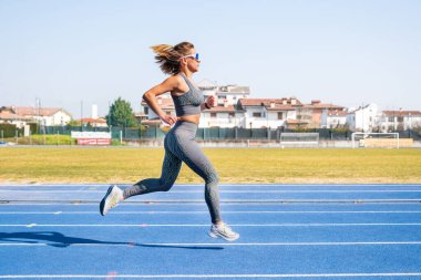 Genç bir kadın mavi bir pistte koşuyor, güneşli bir günün tadını çıkarıyor.