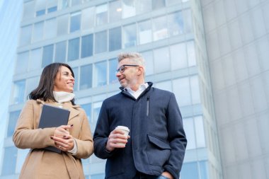 Finans bölgesindeki şirket binalarının önünde yürürken iki iş adamı keyifli bir konuşma yapıyorlar.