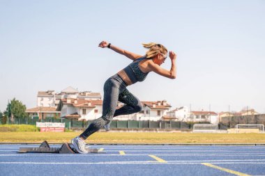 Genç bayan sporcu, güneşli ve aydınlık bir günde koşu parkurunun başlangıç noktalarından atlıyor.