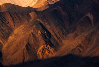 Güneş ışığıyla kaplı bir dağ yamacında taş dokusu. Gölgeler ve röfleler. Ladakh, Hindistan.