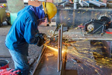 Bir işçi çelik levhanın yüzeyini öğütmek için öğütme makinesini kullanır. Sonra onu çelik boruya monte eder. Bir sanayi fabrikasında..