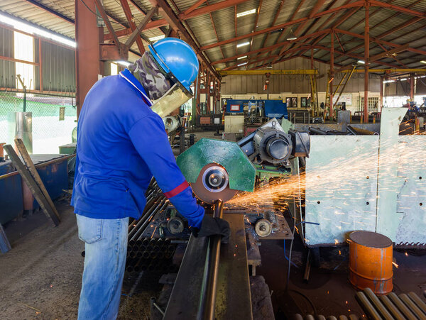 Industrial Worker Cutting Steel Pipe with a CUT-OFF Machine in a Factory, Wearing a Safety Helmet, Gloves, and Protective Gear, Sparks flying from the Cutting Process.