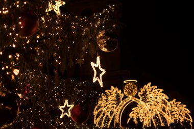 Arka planda aydınlanmış bir meleği ön planda süslenmiş bir süs dalıyla gösteren güzel bir görüntü. Karanlık bir zemindeki bu şenlik sahnesi Noel tebrik kartı için idealdir. Sıcak ve kişisel bir mesaj için boşluk bırakır..