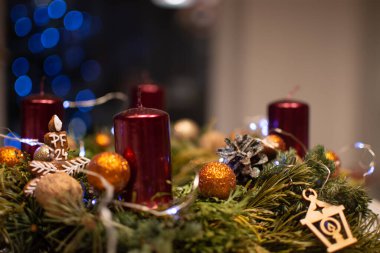 A traditional Christmas Advent wreath made of pine needles, adorned with a few ornaments and four candles. The wreath is set against a soft backdrop of twinkling blue lights, creating a serene holiday atmosphere. clipart