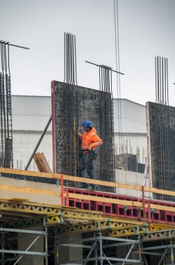 Bratislava, Slovakya - 15 Nisan 2025: İnşaat işçisi mavi bir şapka takıyor, inşaat sahasında çelik inşaat demirleri üzerine çalışıyor.