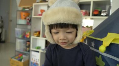 Mutlu küçük çocuk şapka takıyor ve evde gülümsüyor, yavaş çekim sahnesi.