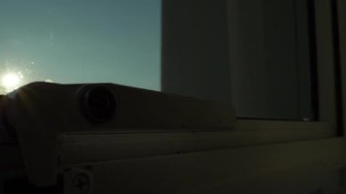 Açık pencereden açık gökyüzü görüntüsü kahverengi perdeli, içeriden yavaş çekim sahnesine bakıyor