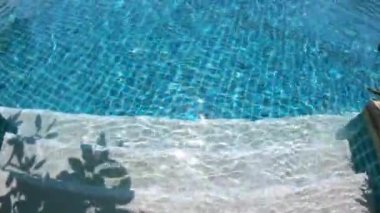 Güneşli bir günde yüzme havuzuna doğru merdivenlerden inerken 4K hareket sahnesinde suyun yüzeyinde.