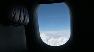 Uçak yolculuğu, açık mavi gökyüzünde güzel bulutlarla uçarken, uçağın penceresinden manzaraya bakar.