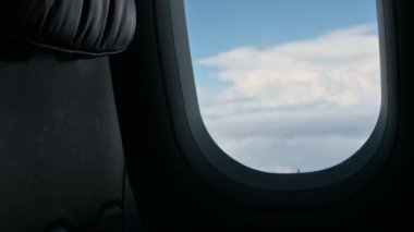 Uçak yolculuğu, açık mavi gökyüzünde güzel bulutlarla uçarken, uçağın penceresinden manzaraya bakar.