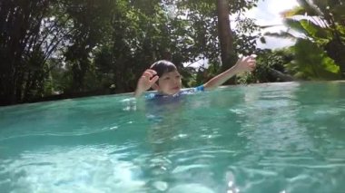 Havuza yüzen tatlı çocuk, güneş ışığıyla birlikte suyun yüzeyinde.