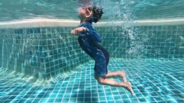 Havuza yüzen tatlı çocuk, güneş ışığıyla birlikte suyun yüzeyinde.