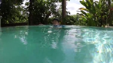 Havuza yüzen tatlı çocuk, güneş ışığıyla birlikte suyun yüzeyinde.
