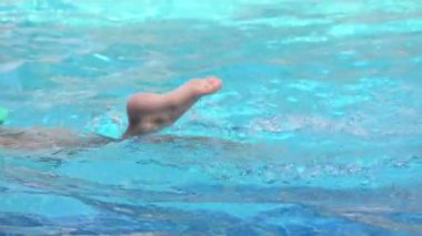 Havuza yüzen tatlı çocuk, güneş ışığıyla birlikte suyun yüzeyinde.