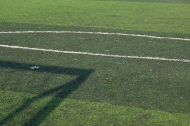 Yapay yeşil çimen çim sahası futbol sahasında siyah lastik tanecikler doluyor ve futbol kalesinin gölgesi.