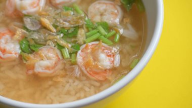 Sarı zemin üzerinde beyaz kâse içinde karides olan pirinç çorbası.
