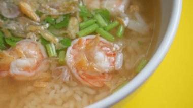 Sarı zemin üzerinde beyaz kâse içinde karides olan pirinç çorbası.