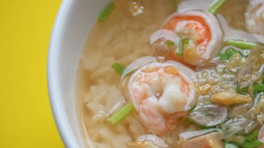 Sarı zemin üzerinde beyaz kâse içinde karides olan pirinç çorbası.