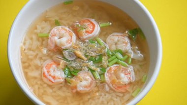 Sarı zemin üzerinde beyaz kâse içinde karides olan pirinç çorbası.