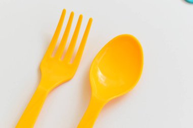 Beyaz arka planda izole edilmiş sarı kaşık ve çatal, piknik için plastik çatal bıçak.