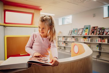 Little girl reading in librarys creative space. High quality photo. Learning joy concept. Love reading concept.  clipart