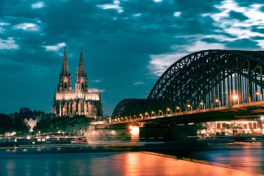 Akşamları Köln Katedrali ve Hohenzollern Köprüsü bulutlu gökyüzüne karşı yapay aydınlatma ile