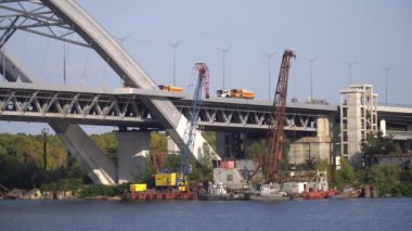 Kyiv 'de bir Podolsky Köprüsü inşaatı. Köprüde kamyonlar sürüyor. İnşaat vinçleri kıyıya yakın nehirde duruyor.