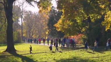 Sonbahar parkında yürüyen bir grup insan.