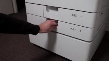 Bir ofis çalışanı yazıcı tepsisinden bir deste kağıt çıkarır.