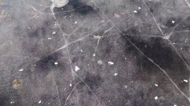 Donmuş bir kış nehrini kaplayan buzda yürüyorum. Çatlaklar, hava kabarcıkları ve donmuş algler buzda görülebilir.